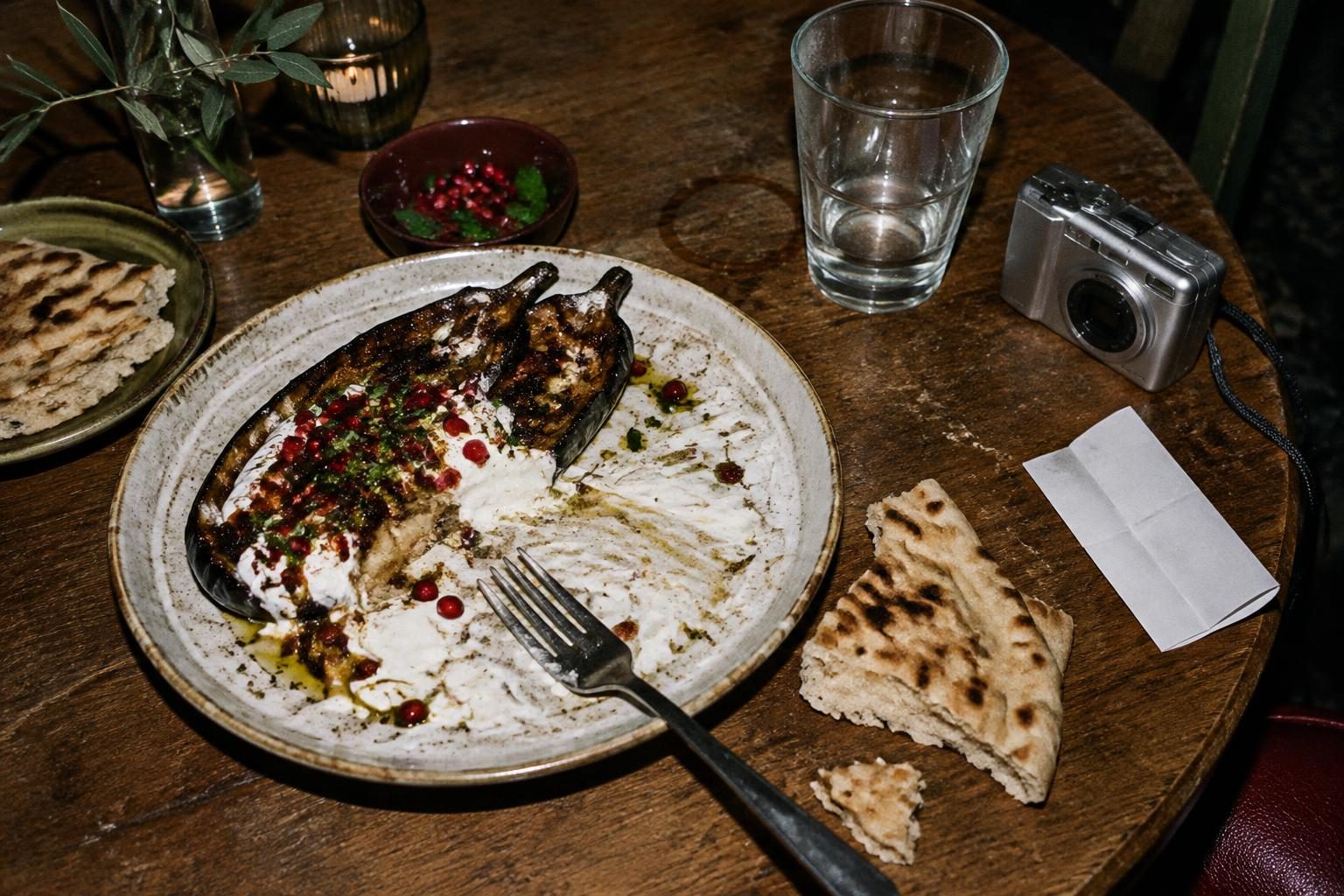 Half-eaten aubergine, torn flatbread and a compact camera after dinner.