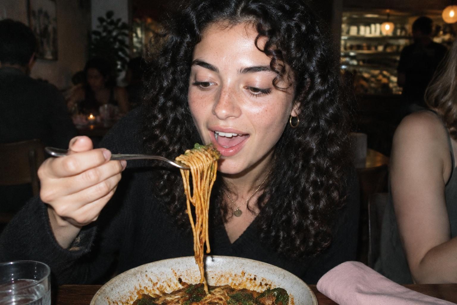 A diner tries a forkful of spicy noodles at a busy restaurant.